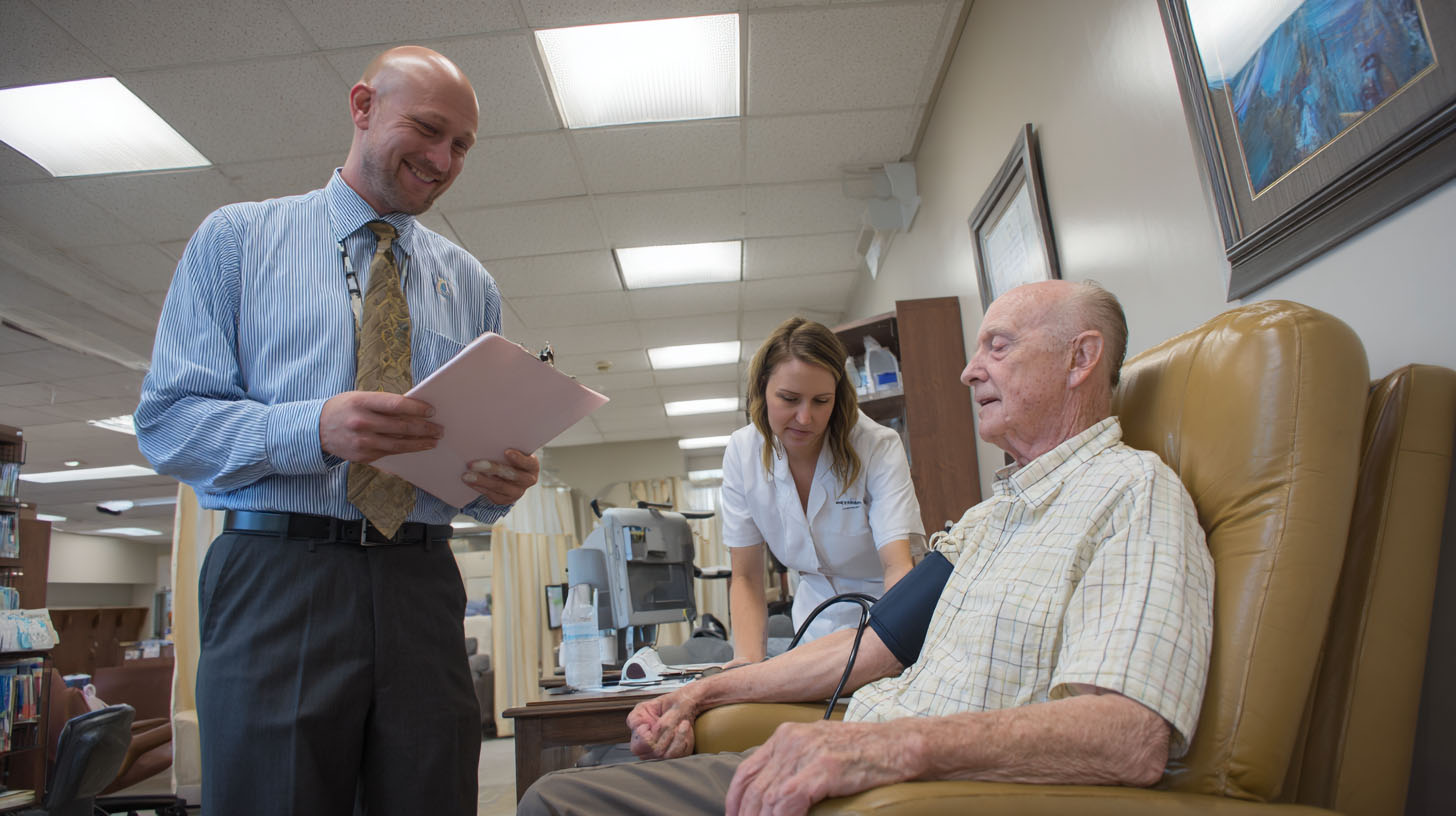 A doctor in a shirt and tie and nurse are standing around a patient
